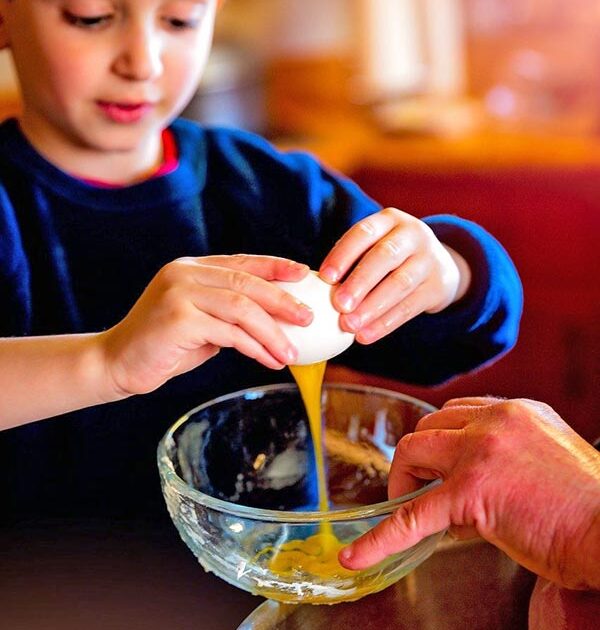 Child breaking an egg whilst baking with Food Thoughts baking ingredients