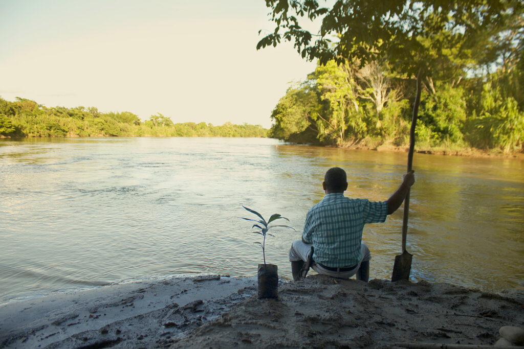 fair trade cocoa farmer sitting at the side of a river