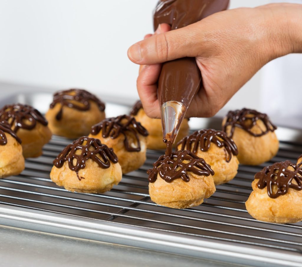 woman's hand piping chocolate sauce on easy chocolate profiteroles