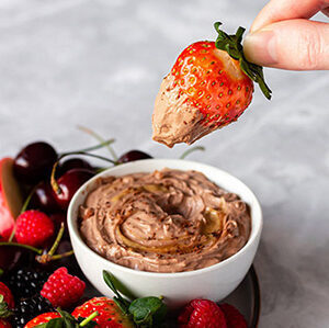 hand dipping a strawberry in a chocolate peanut butter dip