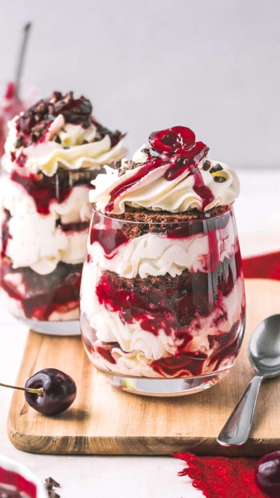 black forest gateau cake in a glass with a spoon and fresh cherries