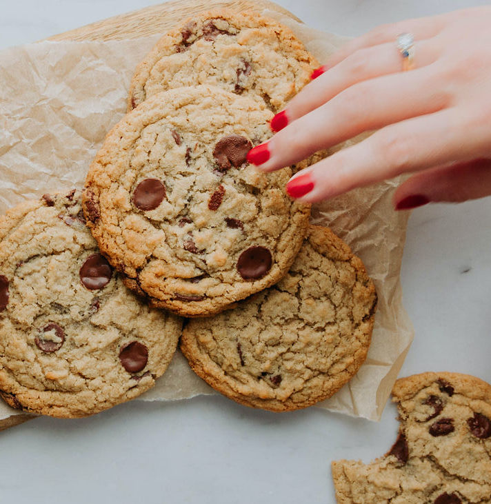 woman's hand picking a vegan chocolate chip cookie from a pile of cookies